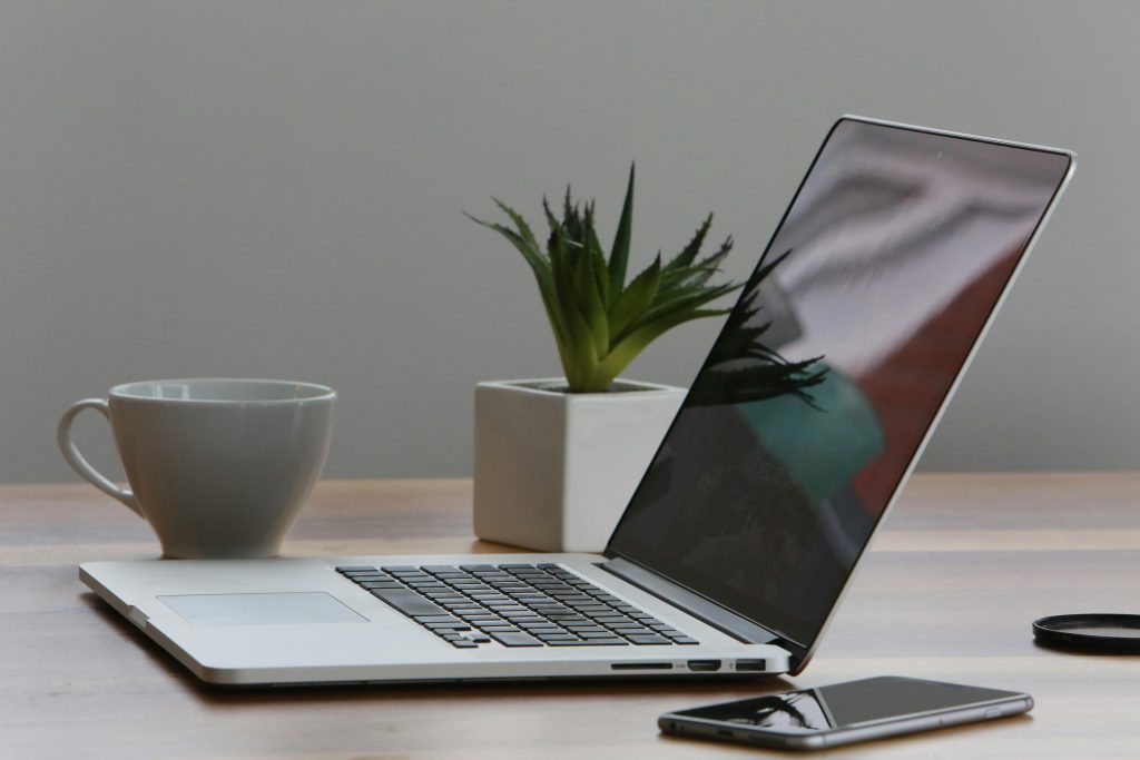 A laptop and phone on a pristine desk with a small green plant.