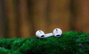 Apple AidPods om some green grass with a blurred fence int he background